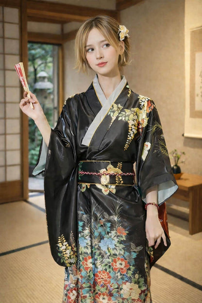 Femme en kimono noir orné de fleurs colorées, posant dans un intérieur japonais traditionnel, avec un éventail à la main