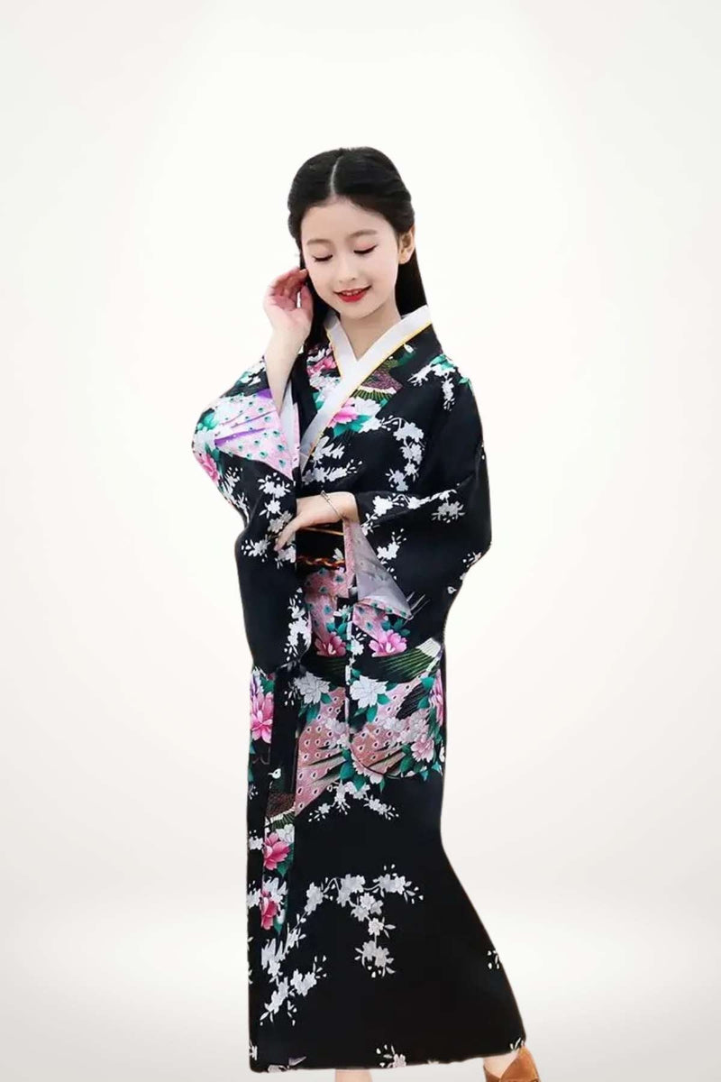 Fille en kimono noir orné de fleurs roses et blanches, posant avec élégance sur fond clair