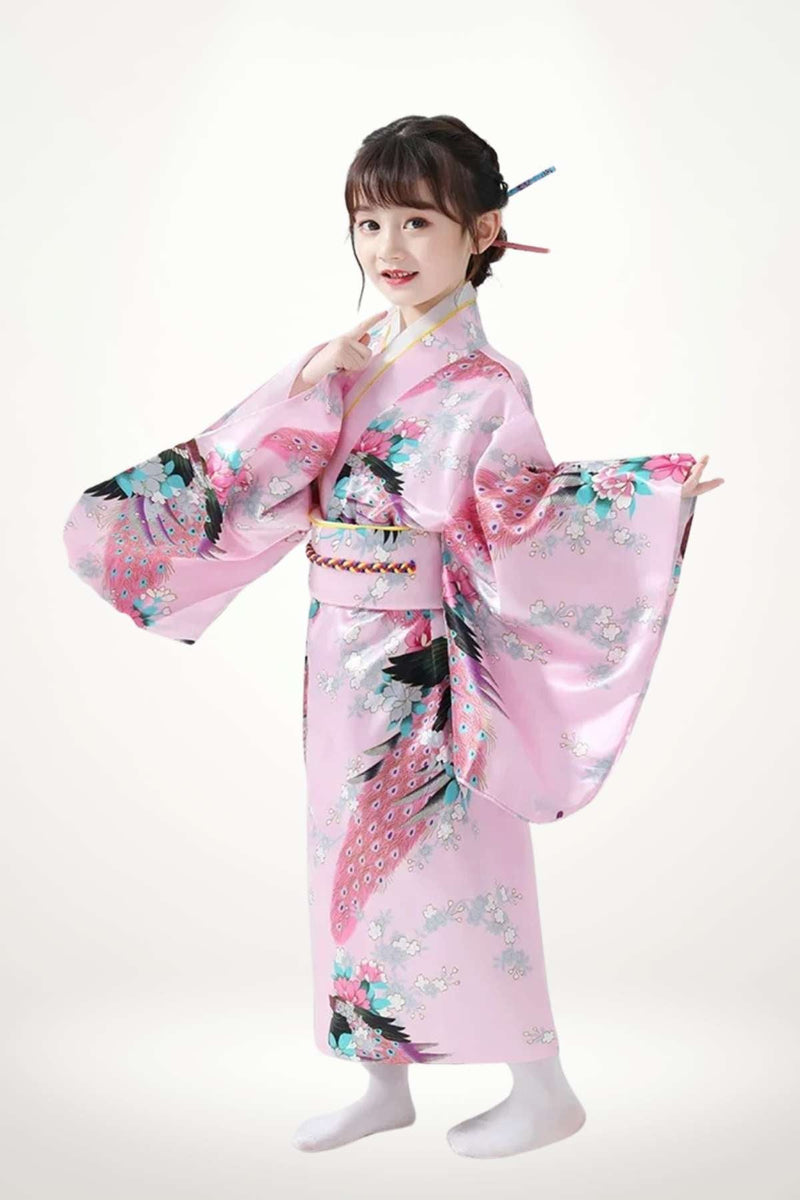 Une petite fille souriante porte un kimono rose orné de motifs floraux colorés et de manches larges