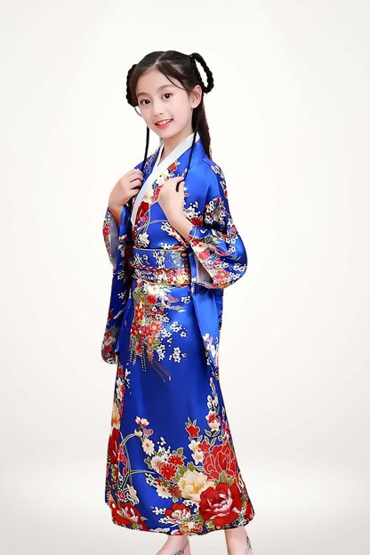 Fillette souriante en kimono bleu orné de fleurs colorées, posant avec grâce sur fond clair