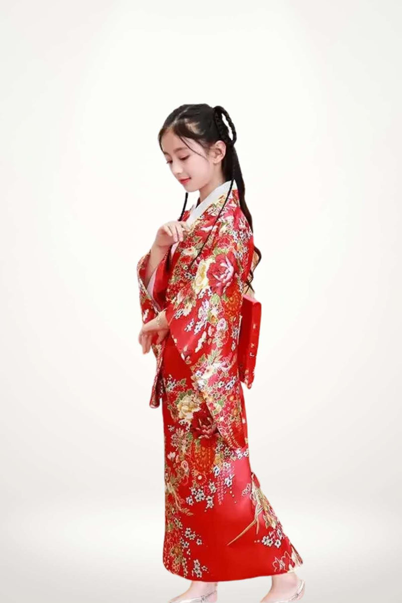 Fillette en kimono rouge orné de fleurs, se tenant de profil avec un décor neutre en arrière-plan