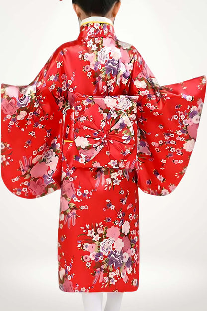 Une fillette porte un kimono rouge à fleurs colorées, avec des manches larges et un obi décoratif à l'arrière