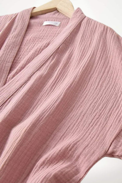 Kimono en gaze de coton rose, avec des textures plissées et des manches larges, suspendu sur un cintre en bois