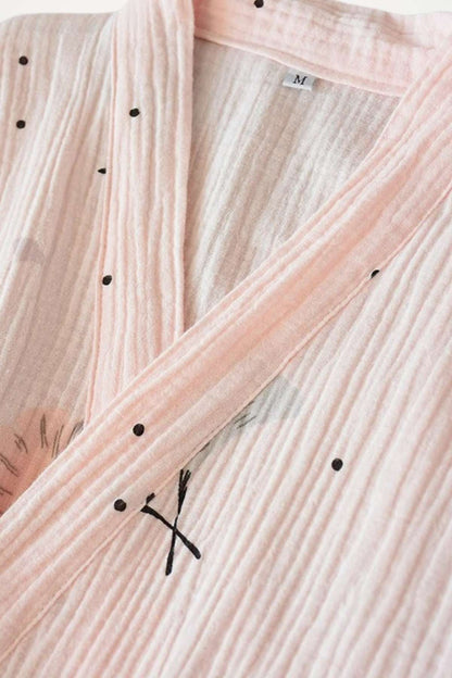 Kimono en gaze de coton rose avec motifs noirs, texture plissée et col ouvert, évoquant douceur et confort