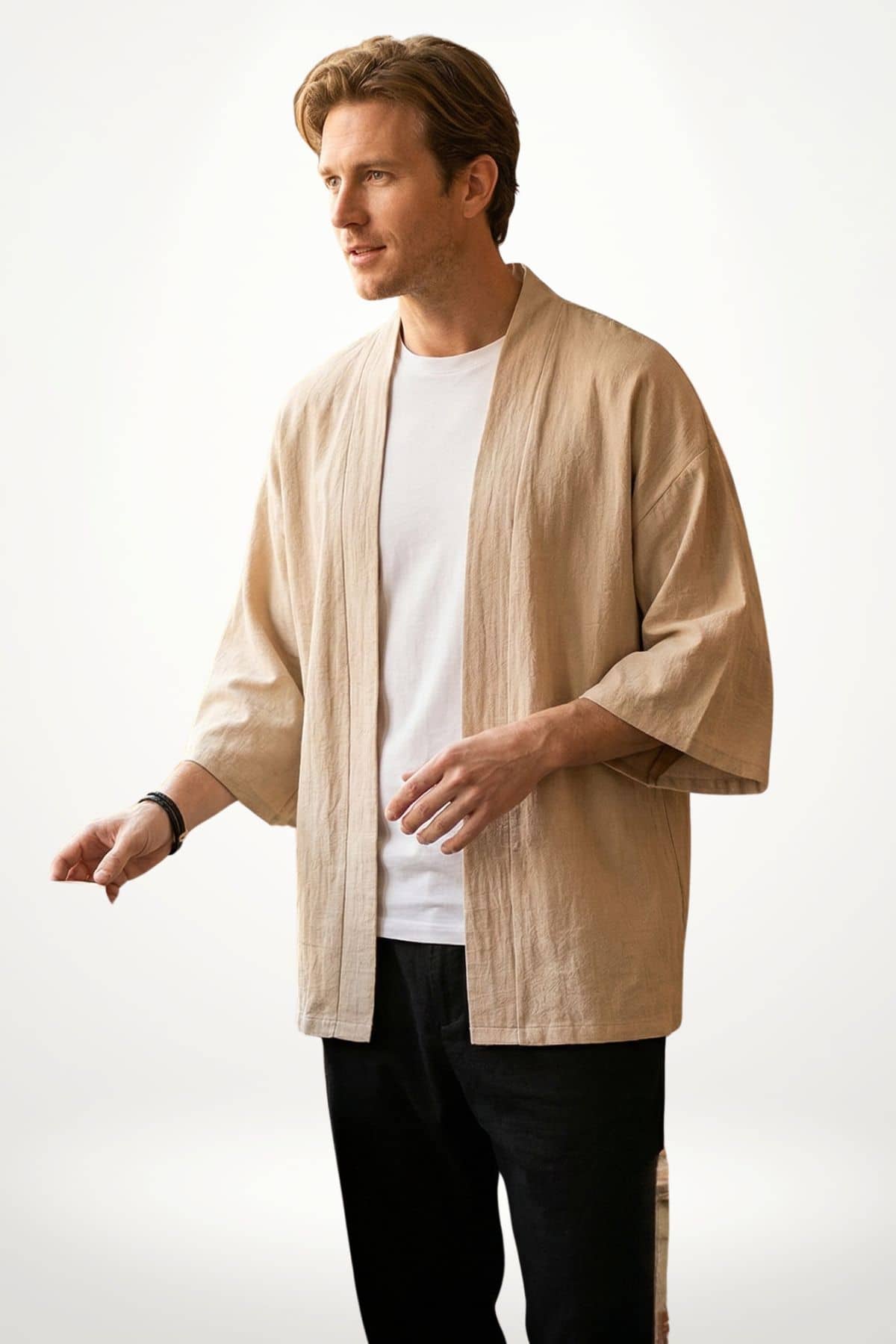 Homme en kimono beige, manches larges, se tenant debout sur fond blanc, avec un t-shirt blanc et un bracelet noir