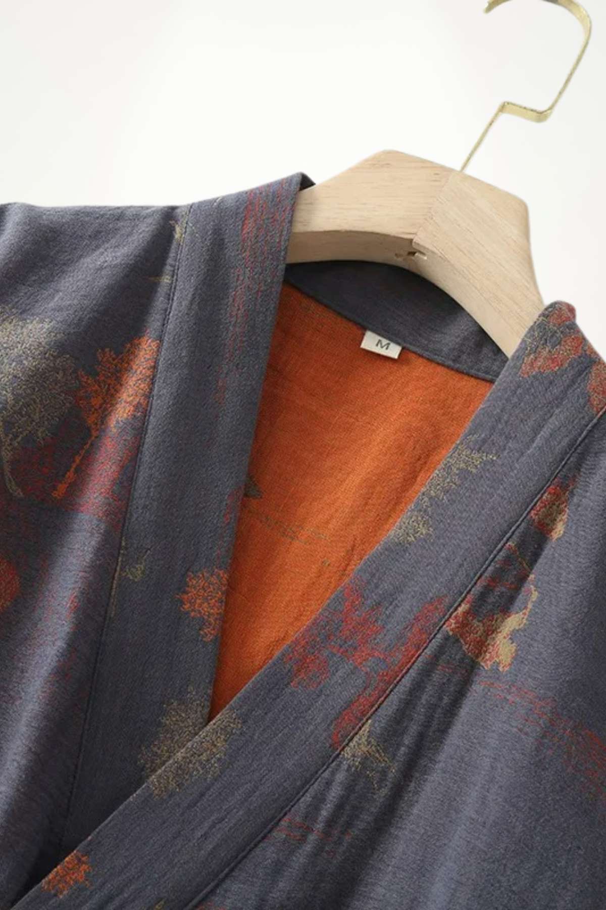 Kimono japonais pour homme en tissu gris avec motifs floraux et doublure orange, suspendu sur un cintre en bois