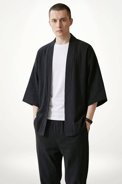 Homme en kimono noir avec un t-shirt blanc, posture décontractée, fond clair et minimaliste
