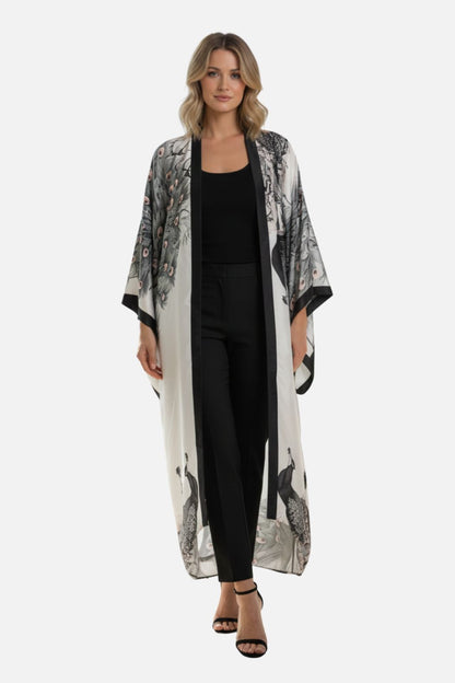 Kimono long blanc avec motifs de paons, porté par une femme en pantalon noir, dans un décor minimaliste