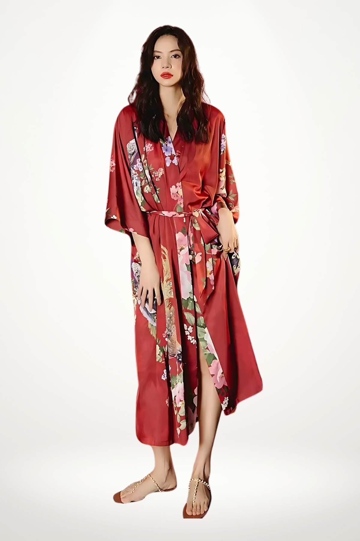 Femme en kimono long rouge satiné avec motifs floraux, posant élégamment sur fond blanc