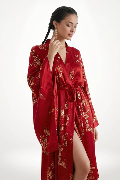 Femme en kimono long rouge en satin, orné de motifs floraux dorés, posant élégamment avec une main sur le visage