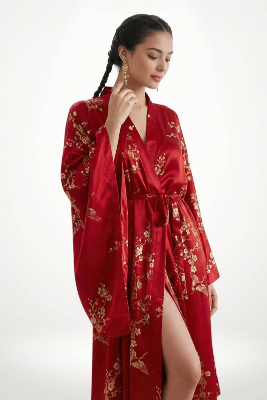Femme en kimono long rouge en satin, orné de motifs floraux dorés, posant élégamment avec une main sur le visage
