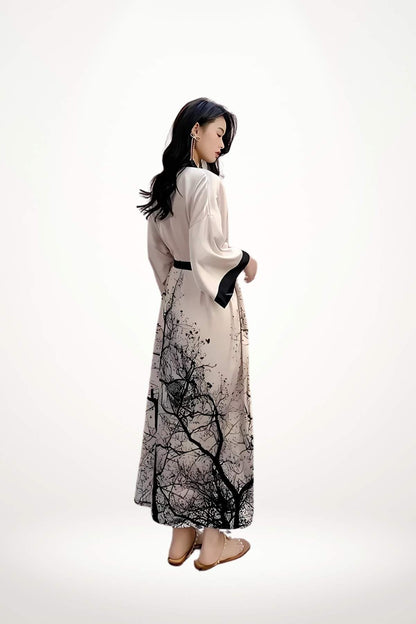 Une femme porte un kimono long en satin beige avec des motifs noirs de branches, dans une posture élégante