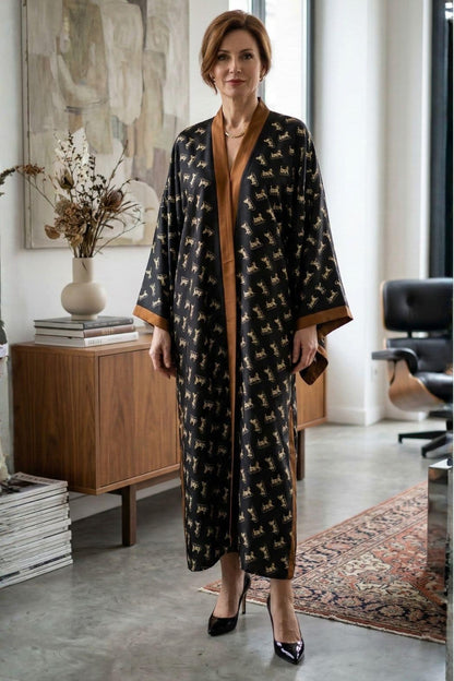 Femme portant un kimono long noir à motifs dorés, avec des détails en satin marron, dans un intérieur moderne