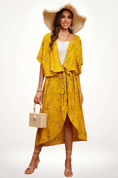 Femme souriante portant un kimono jaune à motifs, chapeau large, sandales et sac en osier, sur fond clair