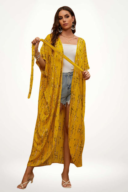 Femme portant un kimono jaune à motifs, avec un débardeur blanc et un short en denim, dans un décor neutre