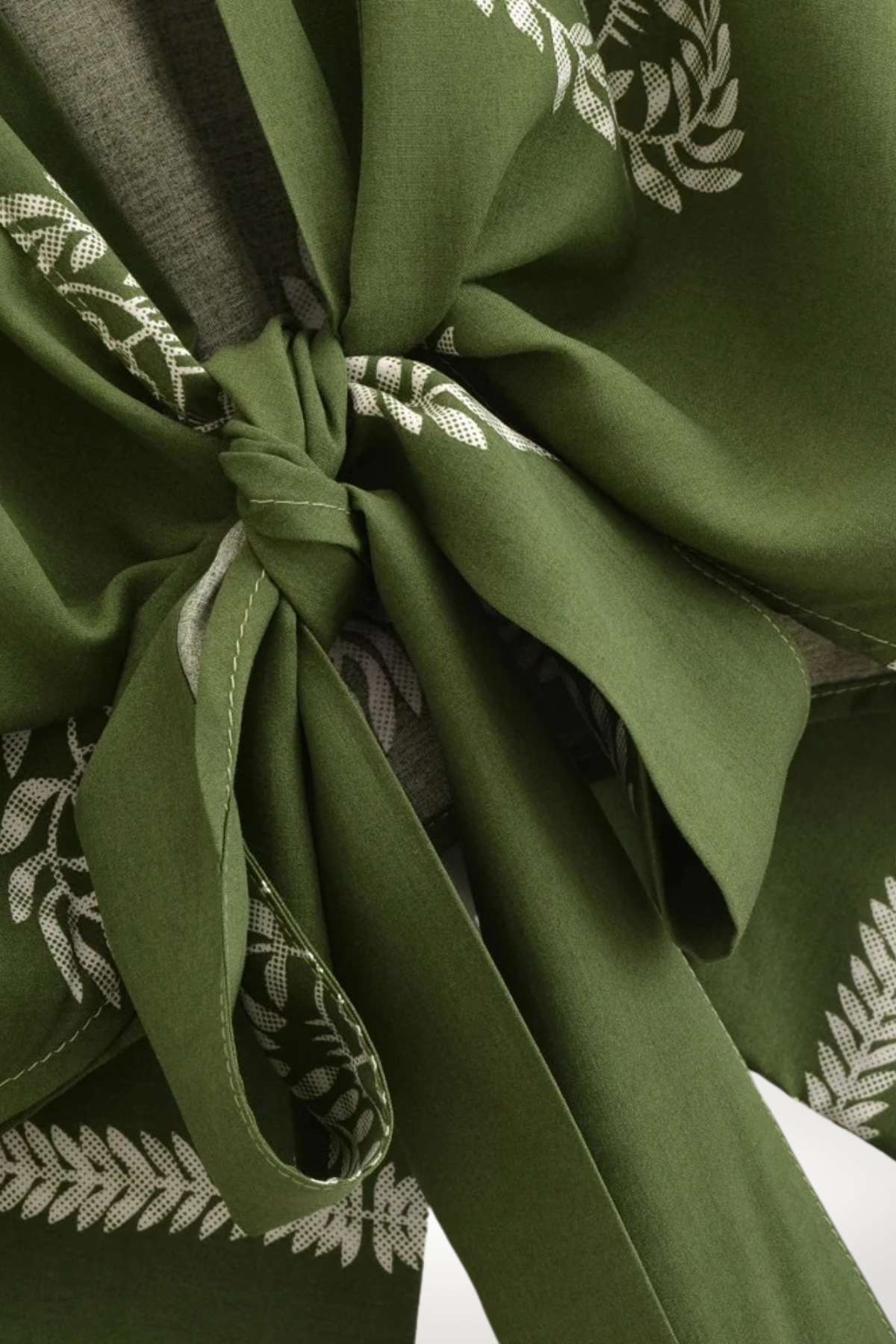 Détail d'un kimono vert olive avec un motif de feuilles blanches, noué élégamment à la taille