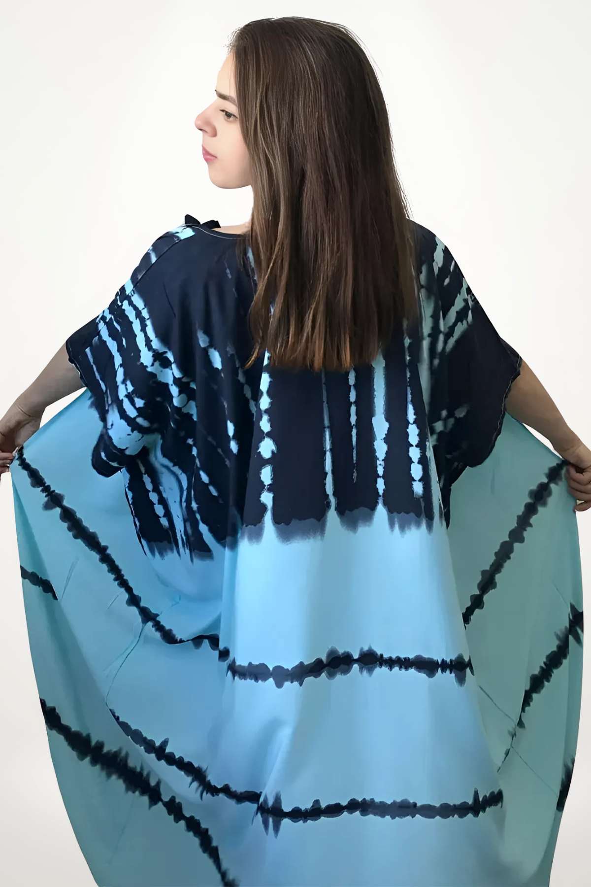 Femme portant un kimono bleu dégradé avec motifs, se tenant de profil dans un décor minimaliste