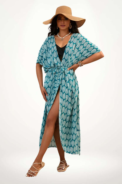 Femme en kimono turquoise à motifs de feuilles, portant un grand chapeau et des sandales, dans un décor lumineux