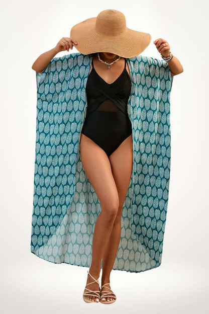 Femme portant un kimono bleu à motifs feuilles, chapeau large et maillot de bain noir, sur fond clair