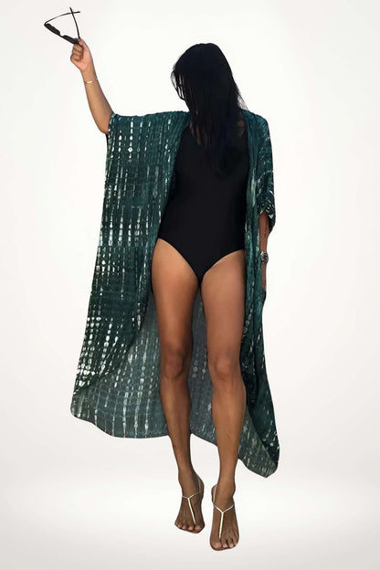 Femme en kimono vert aux motifs irisés, posant avec des lunettes de soleil, sur fond clair