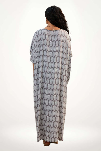 Une femme porte un kimono léger à motifs de feuilles blanches sur fond gris, dans un décor minimaliste