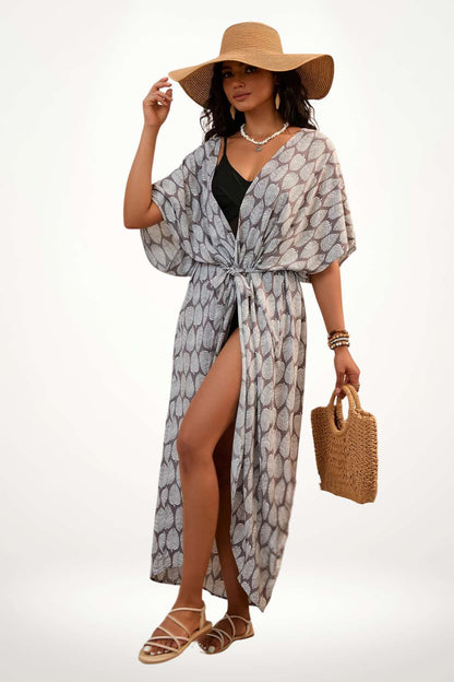 Femme en kimono léger à motifs de feuilles, portant un chapeau large et une pochette en osier, sur fond neutre