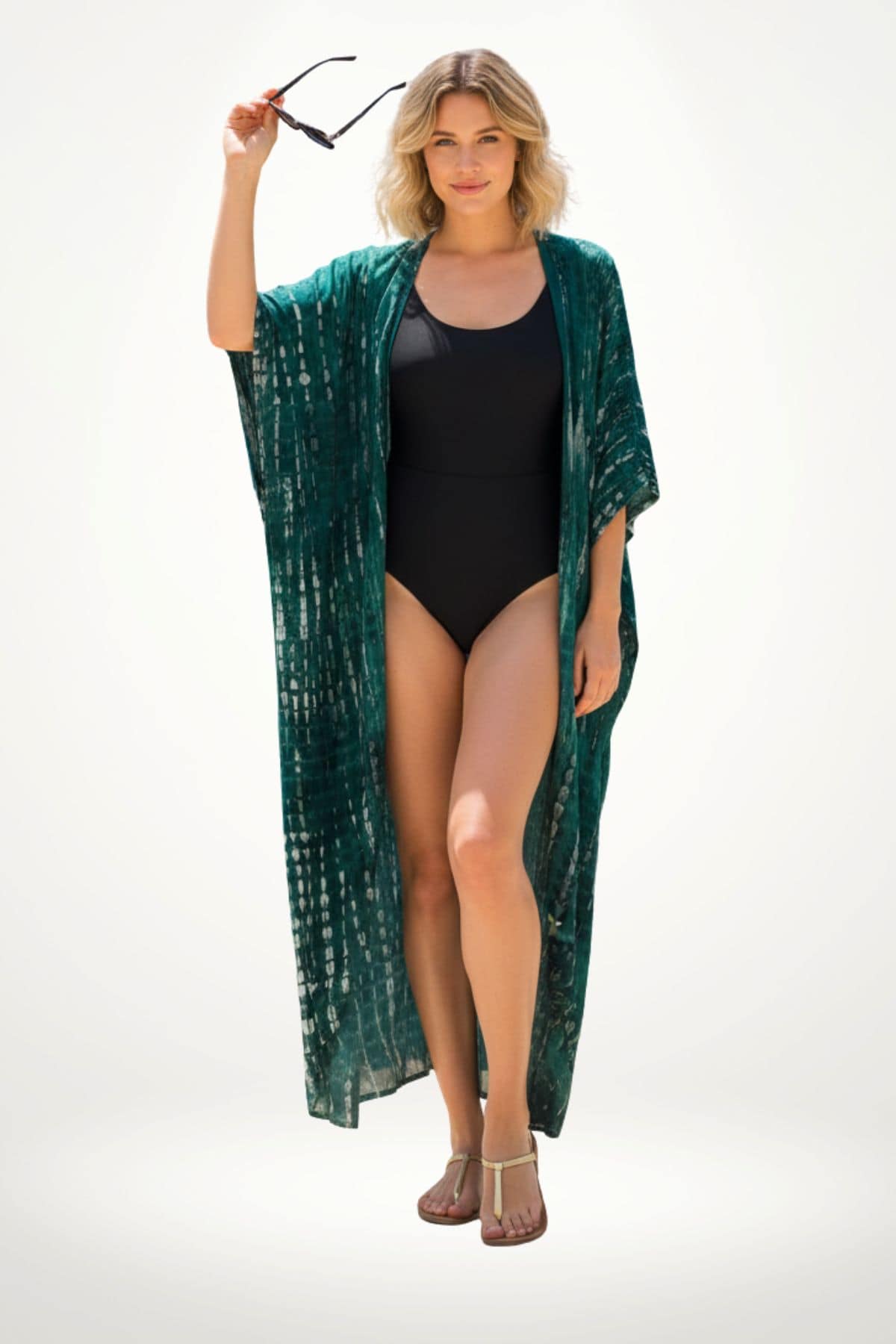 Femme en kimono vert avec motifs, tenant des lunettes de soleil, sur fond clair, vêtue d'un maillot de bain noir