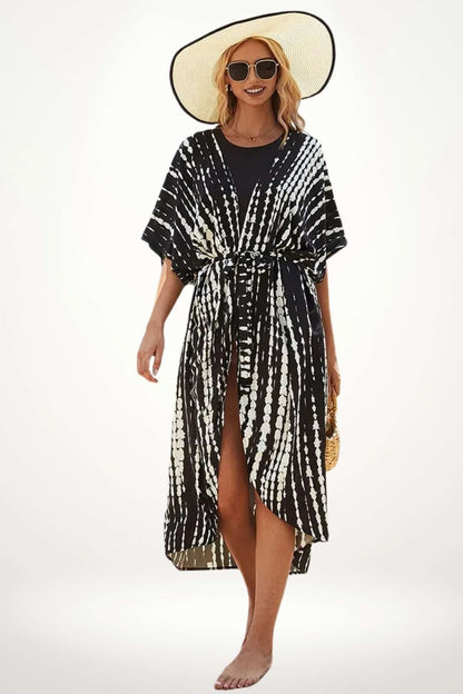 Femme en kimono noir et blanc, motif tie-dye, portant un grand chapeau et des lunettes de soleil, sur fond clair