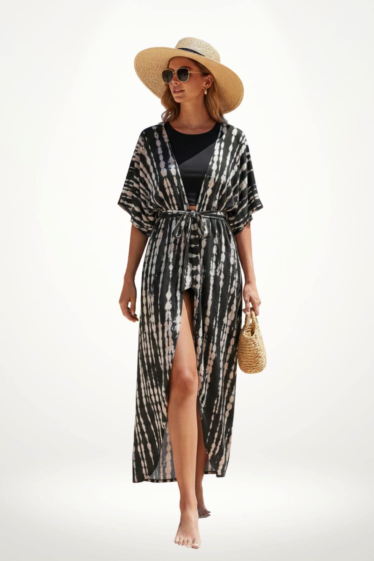Femme portant un kimono noir et blanc à motifs tie-dye, chapeau de paille et sac en osier, sur fond clair