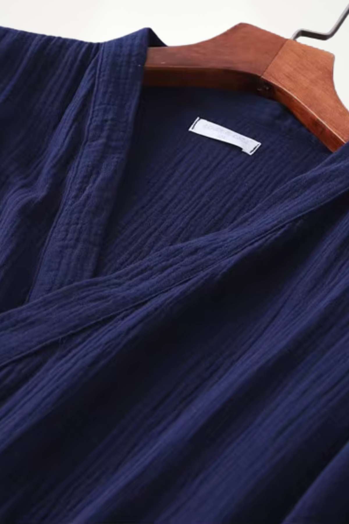 Un kimono en coton de couleur bleu marine, suspendu sur un cintre en bois, avec une texture douce et plissée