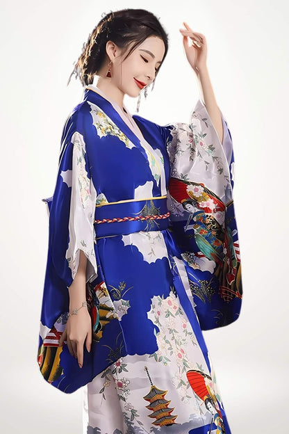 Femme en kimono long bleu royal en satin, motifs geisha et pagode inspirés du kimono traditionnelle, ceinture obi tressée.
