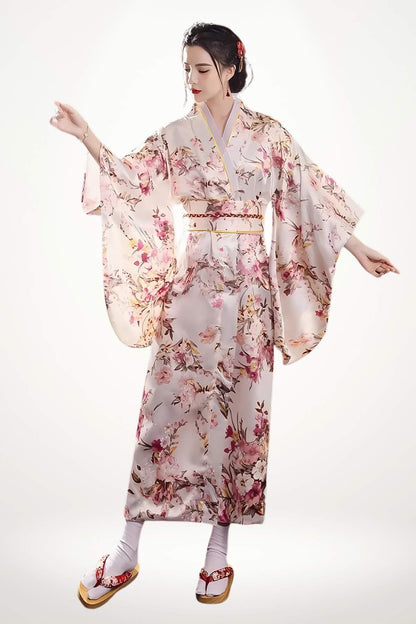 Femme en kimono long en satin pastel à motifs floraux japonais, coupe traditionnelle et ceinture tressée.
