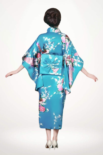 Femme portant un kimono satin bleu orné de fleurs, avec un obi rose, sur fond blanc