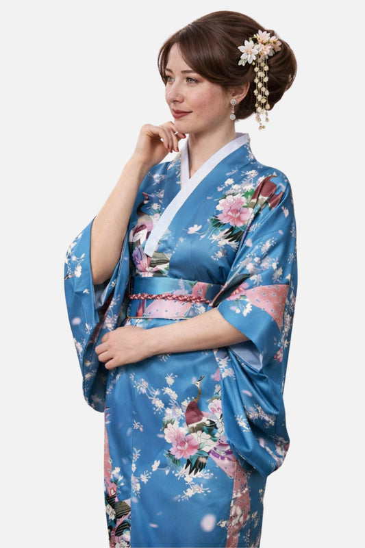 Femme en kimono satin bleu orné de fleurs et d'oiseaux, posant avec une main sur le menton