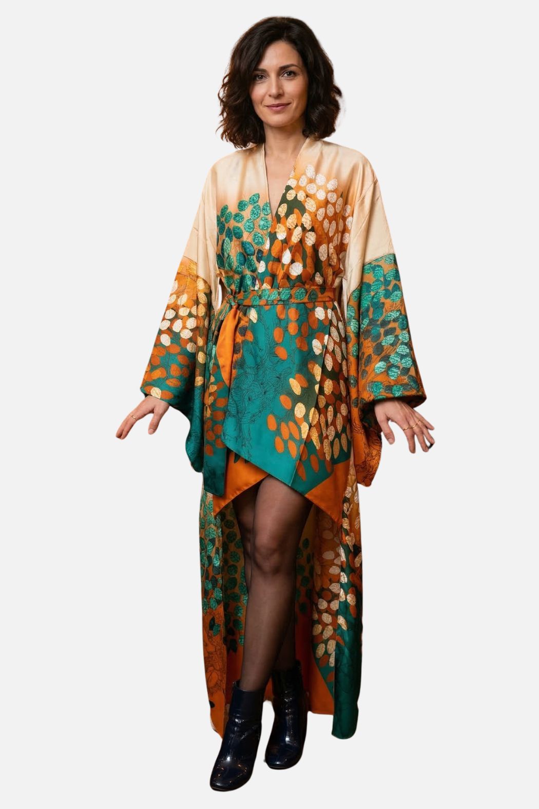 Femme portant un kimono en satin aux motifs oranges et verts, se tenant debout avec un décor neutre