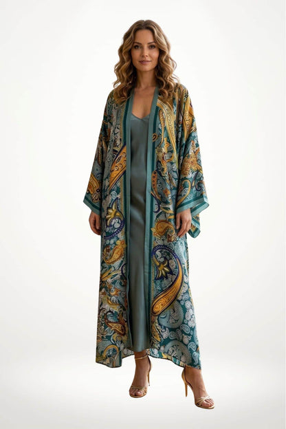Femme portant un long kimono en satin aux motifs colorés, avec des tons verts, dorés et bleu, sur un fond
