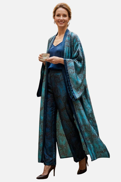 Femme souriante portant un long kimono en satin bleu avec motifs, tenant une tasse dans un décor sobre