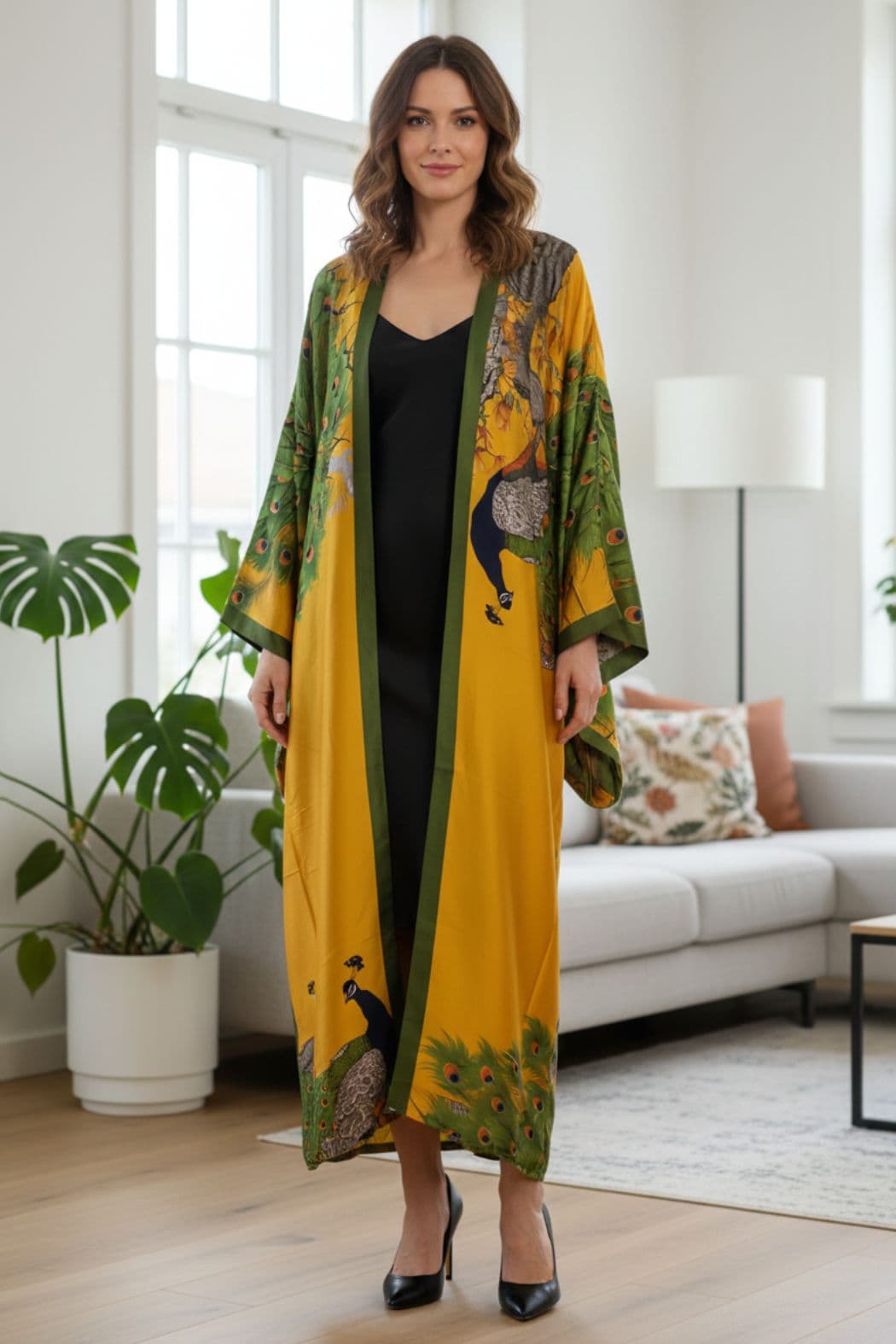 Femme portant un long kimono satin jaune et vert avec des motifs de paon, dans un intérieur moderne et lumineux