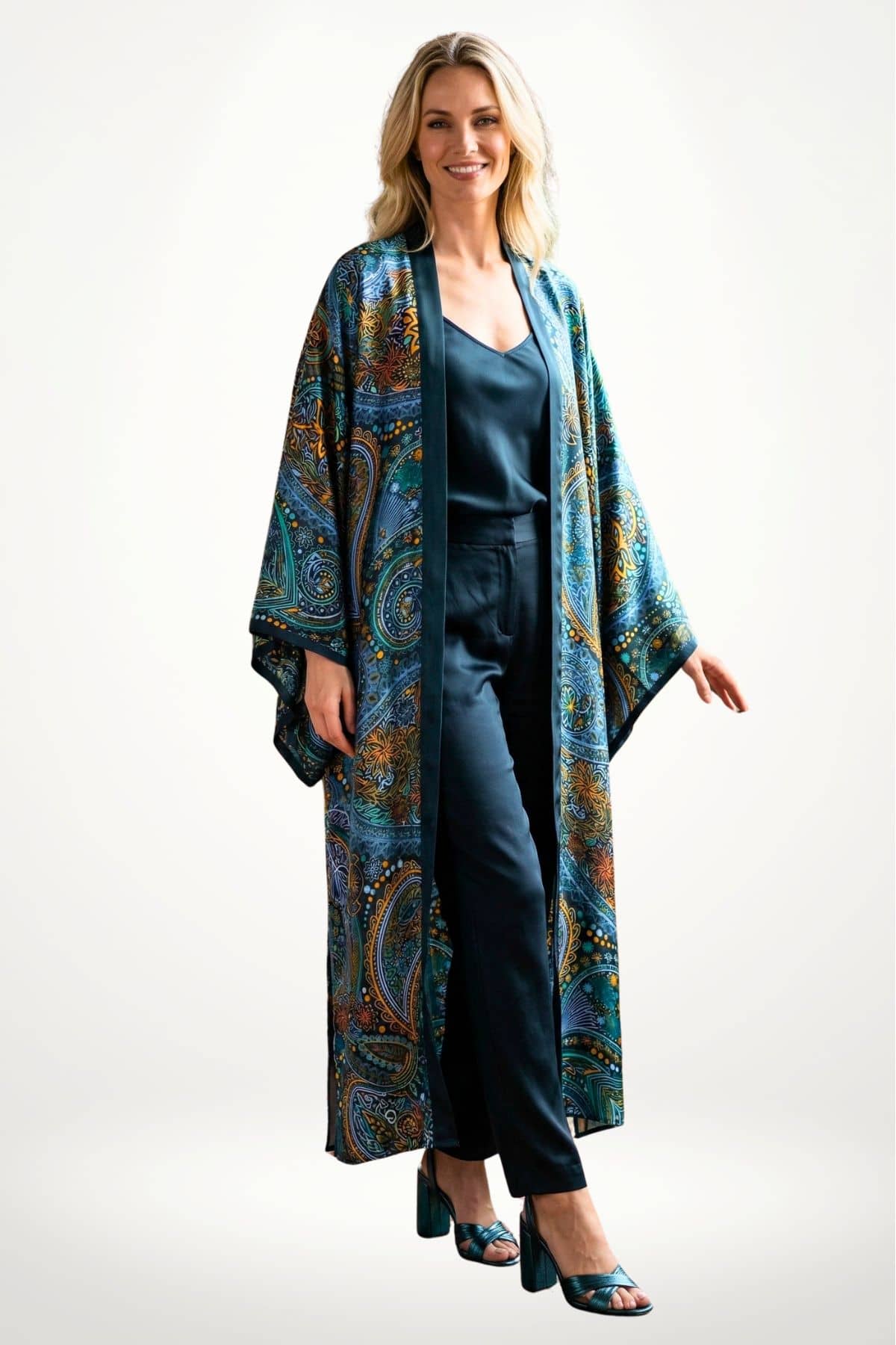 Femme souriante portant un long kimono en satin aux motifs colorés, avec un fond neutre et des chaussures à talons