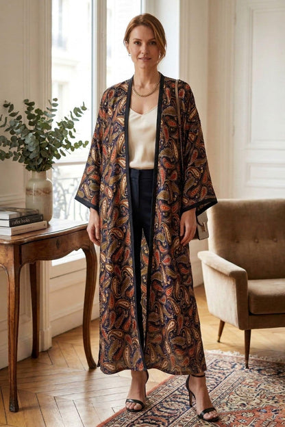 Femme portant un kimono long en satin aux motifs paisley, dans un intérieur lumineux avec un mobilier élégant