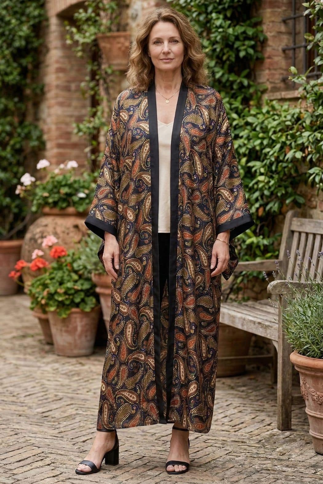 Femme portant un kimono long en satin aux motifs paisley, dans un jardin avec des pots de fleurs colorés