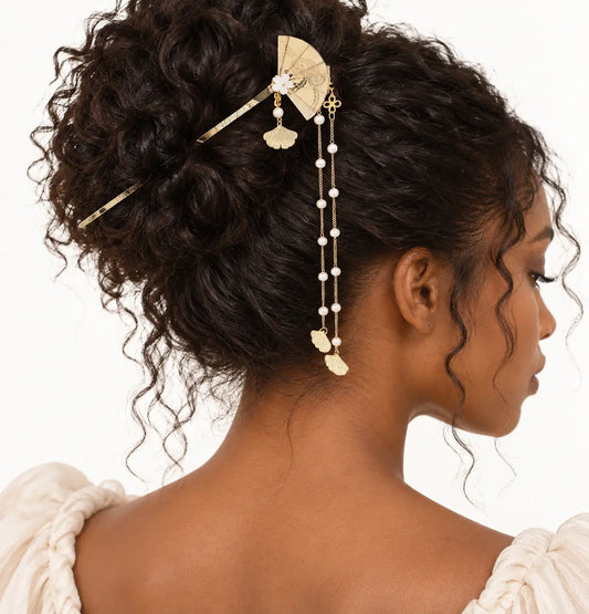 Chevelure bouclée retenue par un bijou doré à éventail et perles pendantes.