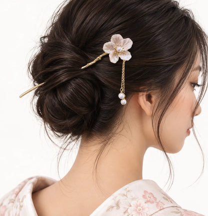 Chignon noir décoré d’une épingle dorée à fleur ivoire et pendentif.