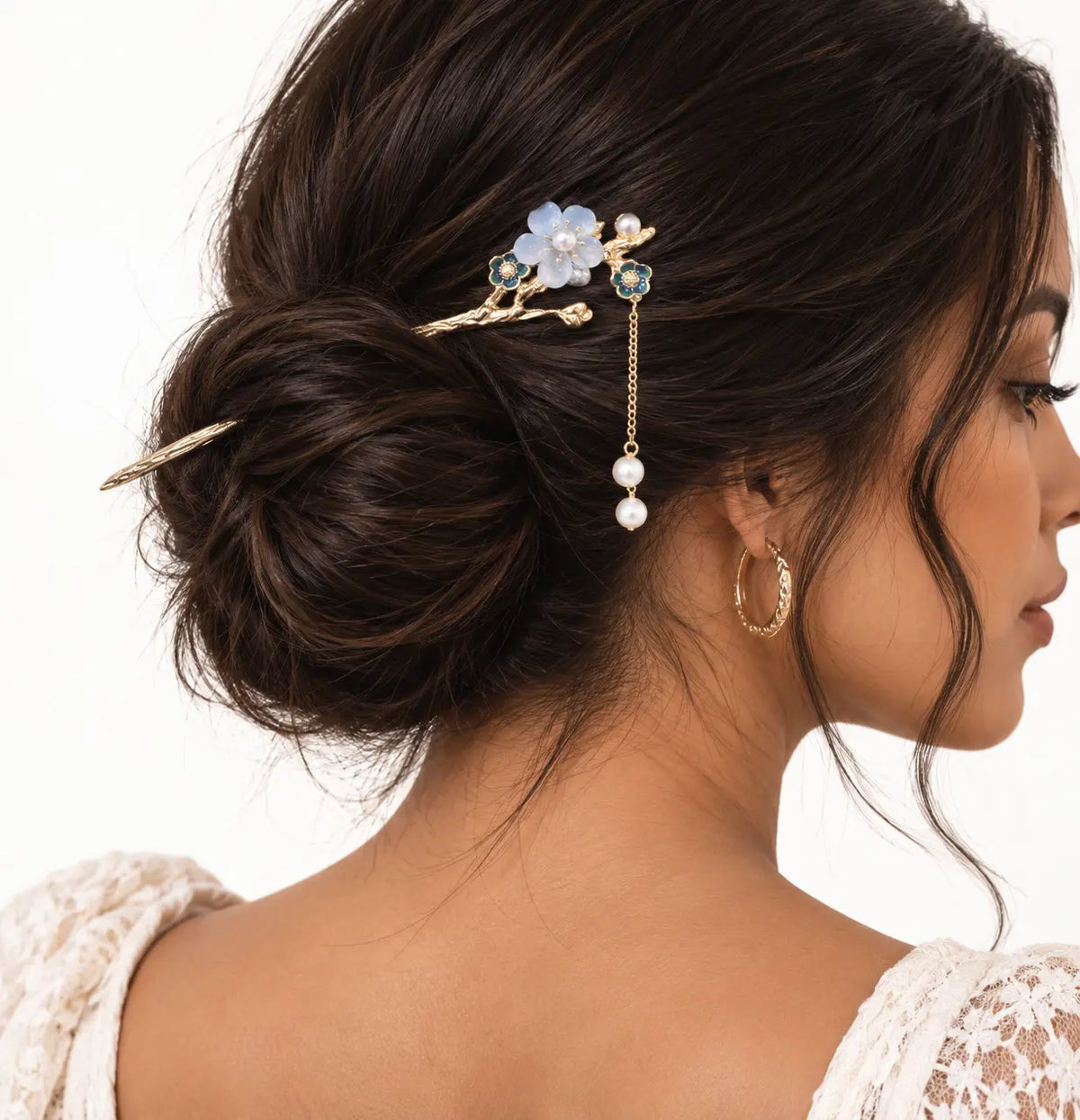 Chignon brun orné d’un bijou doré à petites fleurs bleues.