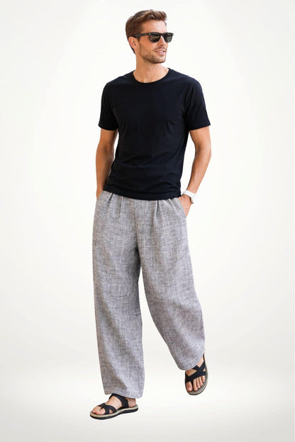 Homme souriant portant un t-shirt noir et un pantalon hakama gris, debout sur fond blanc