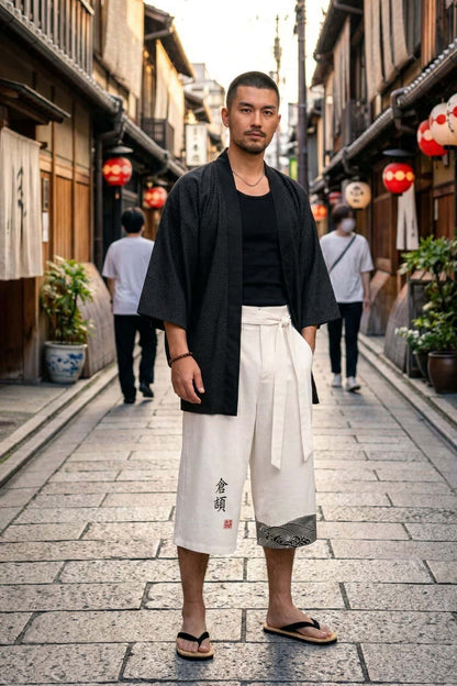 Homme debout portant un pantalon kimono blanc avec un motif noir, décor de rue japonaise