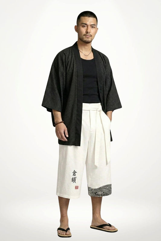 Homme debout portant un pantalon kimono blanc avec un motif noir, décor minimaliste et ambiance zen