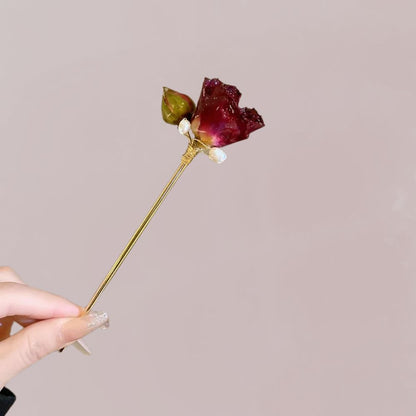 Peigne à cheveux en or avec une rose séchée rouge et un bouton vert, sur fond rose