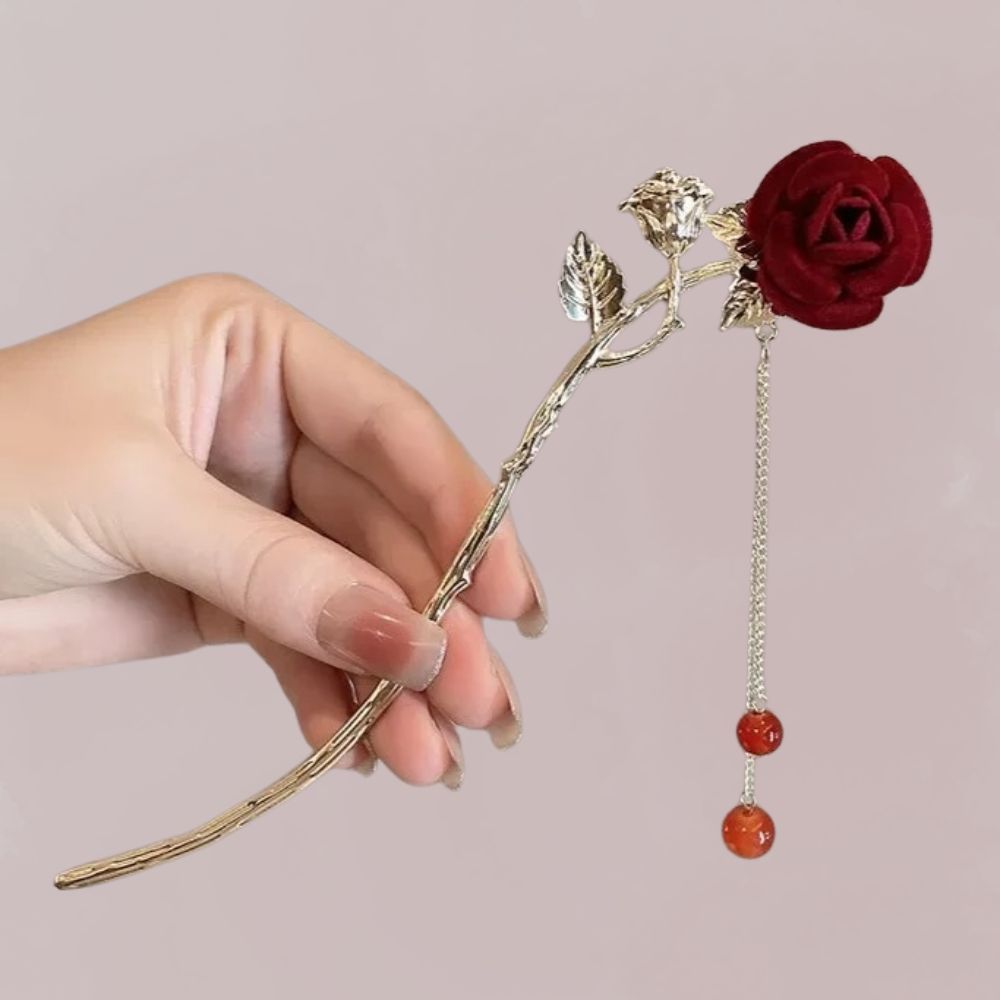 Une épingle à cheveux en métal argenté avec une rose rouge et des perles orange, tenue délicatement par une main