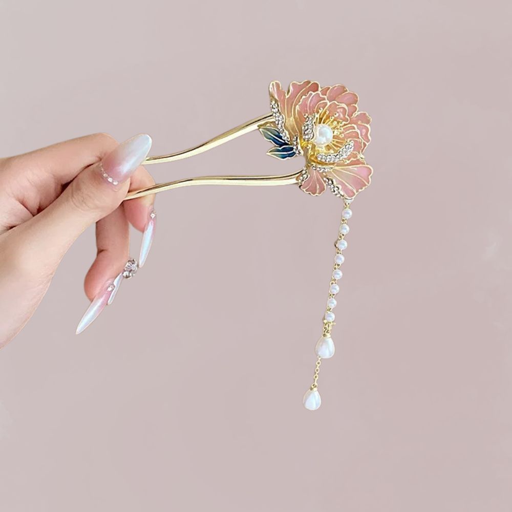 Épingle à cheveux dorée avec une fleur rose et perles, tenue par une main aux ongles décorés